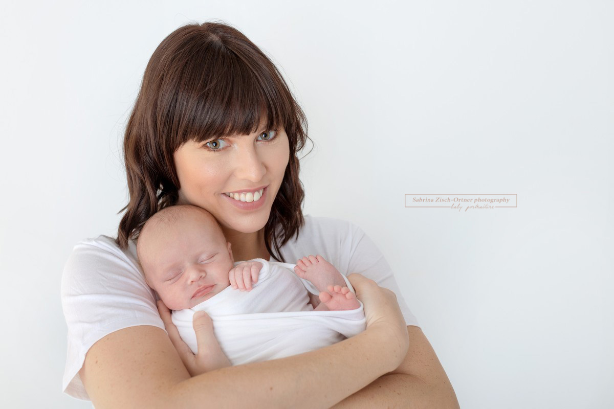 stolze und glückliche Mama mit ihrer frisch geschlüpften Tochter am Arm beim Babyshooting